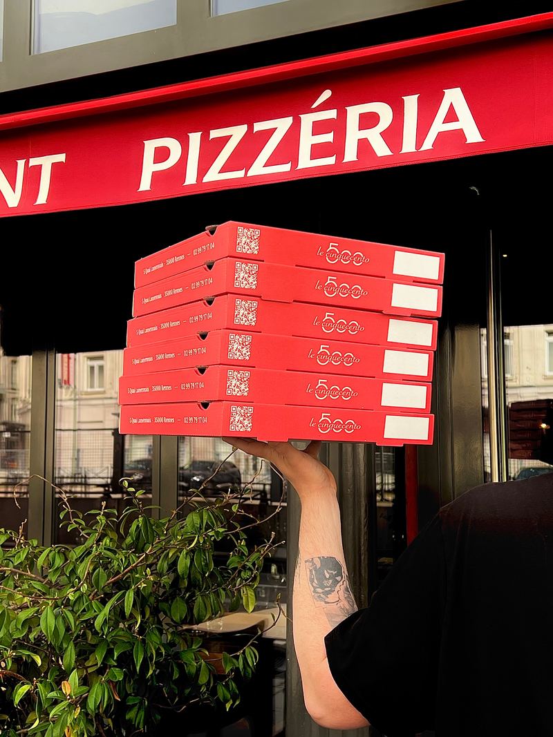 Une pile de boîtes à pizza rouges du Cinquecento devant le store de la pizzéria
