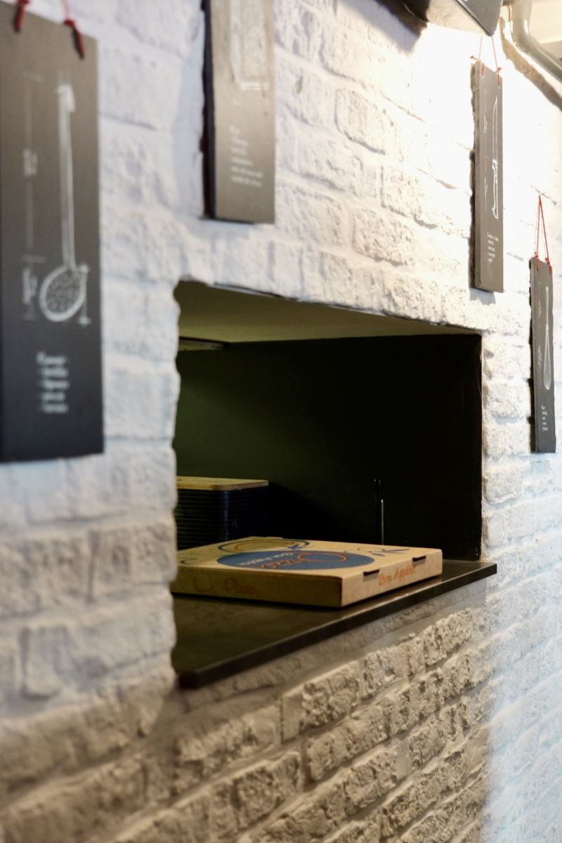 Une boîte à pizza posée sur le passe-plat, dans le mur de brique blanche